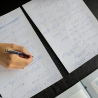 Home Close-up of a student solving mathematical equations with papers and textbook on a table.